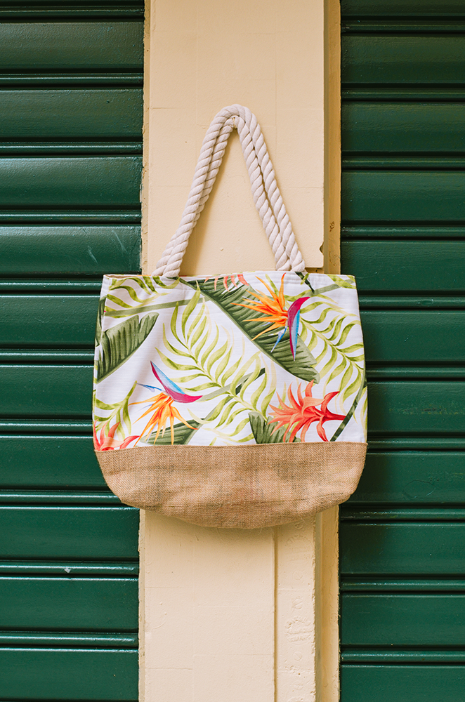 beach tote bag with tropical floral design hanging on a green door.