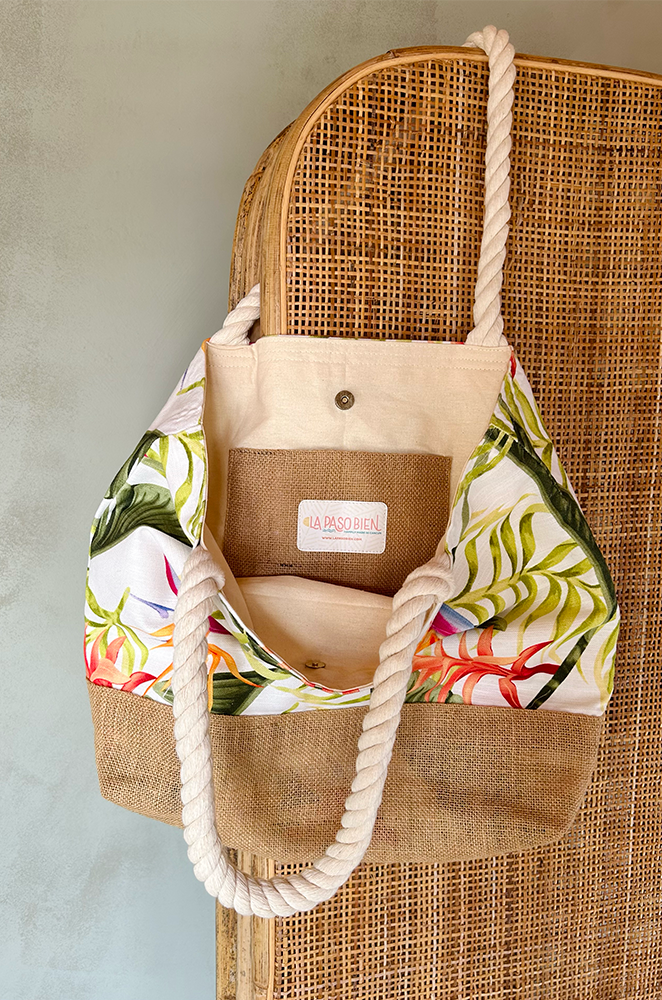 Welcome tote bag with floral pattern and burlap accents hanging from a wicker screen.