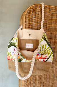 Welcome tote bag with floral pattern and burlap accents hanging from a wicker screen.