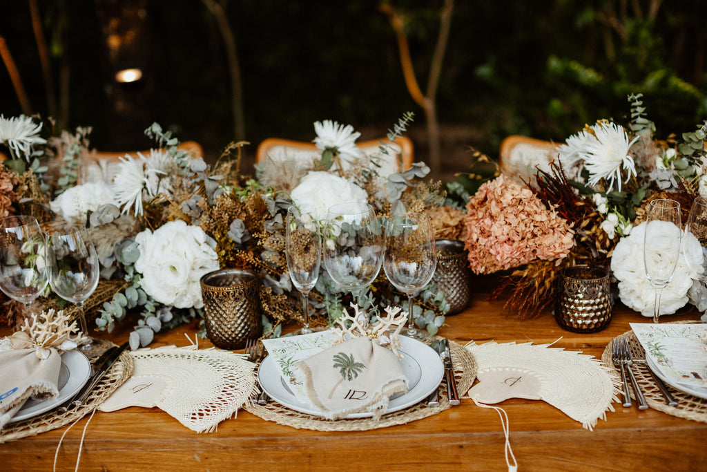 Wedding table decor, personalized woven palm fans and an embroidered napkin are the main focus.