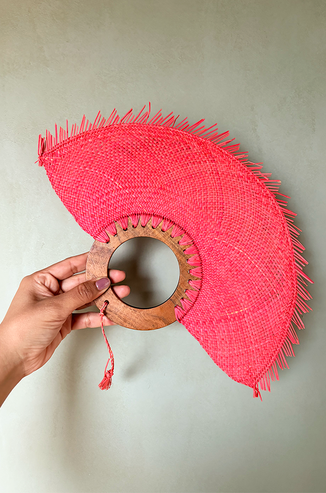 Circular handmade fan in coral color with a neutral wall as background
