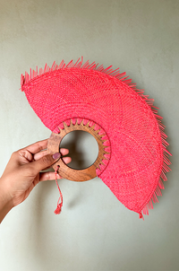 Circular handmade fan in coral color with a neutral wall as background