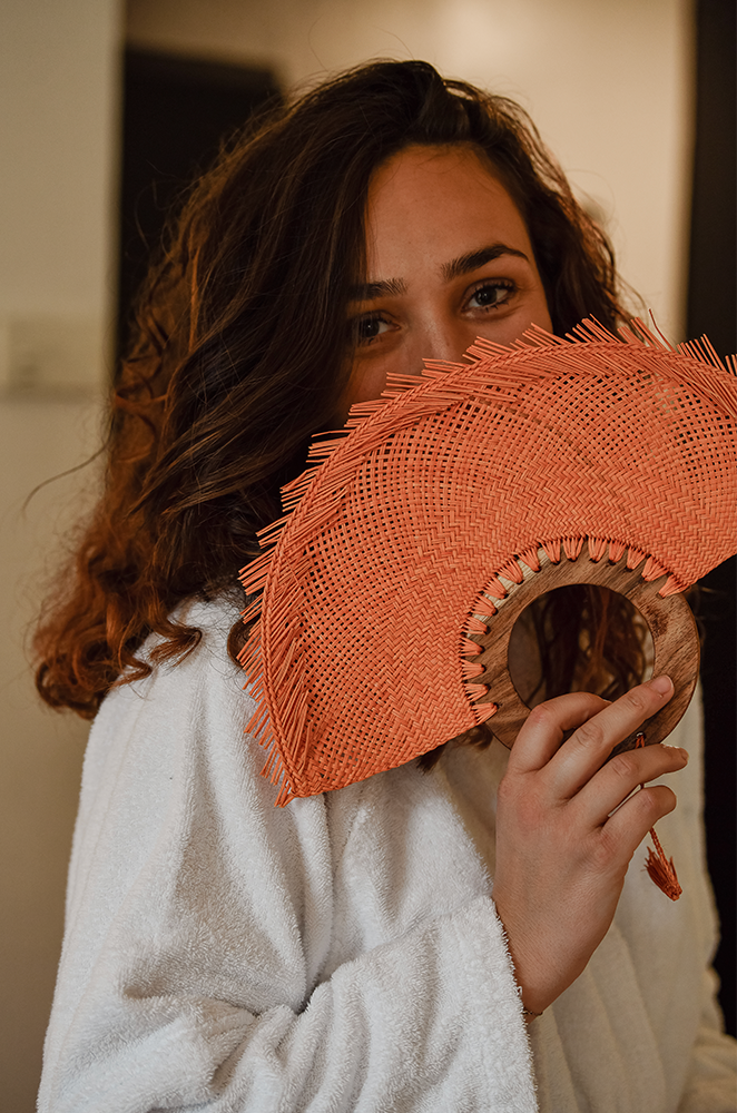 A woman holding a woven palm fan with a circular wooden handle.